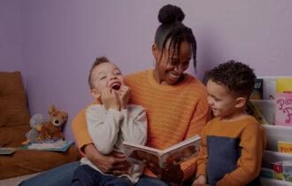 A mother reading a book to two smiling young boys in a cozy, colorful room filled with children's books and plush toys, promoting the joy of reading and family bonding.