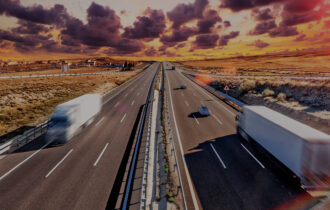Trucks driving on an open highway going in two different directions as the sun sets