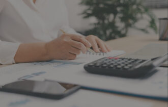 A person sitting at a desk using a pencil to write in a notebook with a calculator nearby.