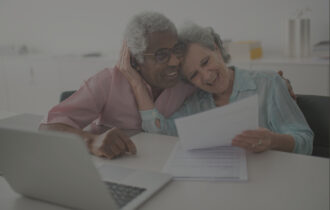 Married couple sitting at a table looking at bills with a computer.