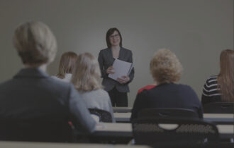 Woman in a suit giving a speech standing in front of an audience