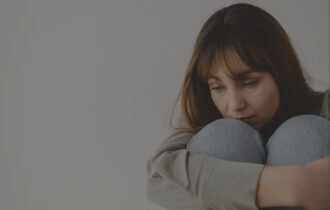 Woman sitting on the ground in front of a white background hugging her knees